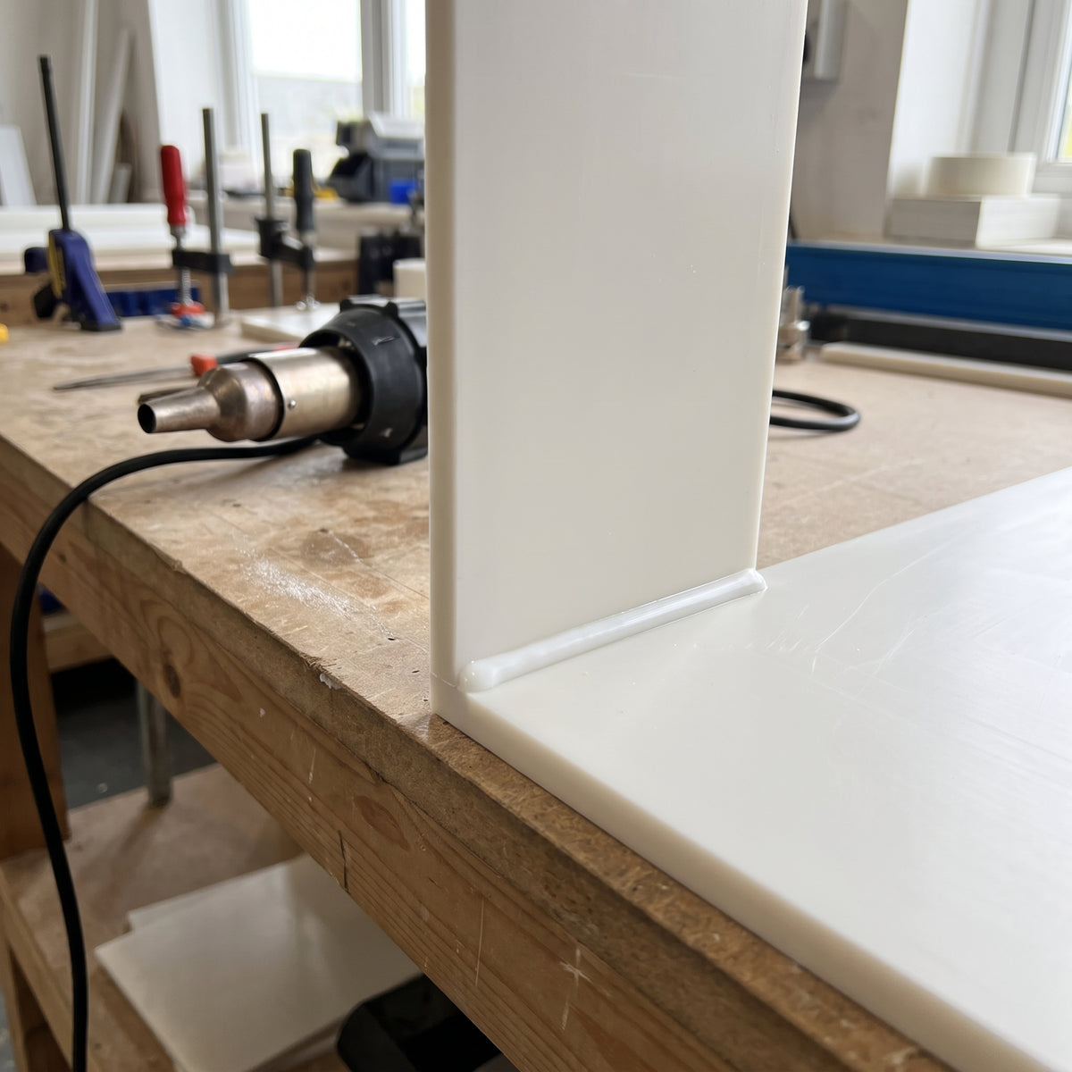 Two natural polypropylene sheets hot-air welded at a right-angle corner with a clean weld bead, plastic welding gun on the workbench