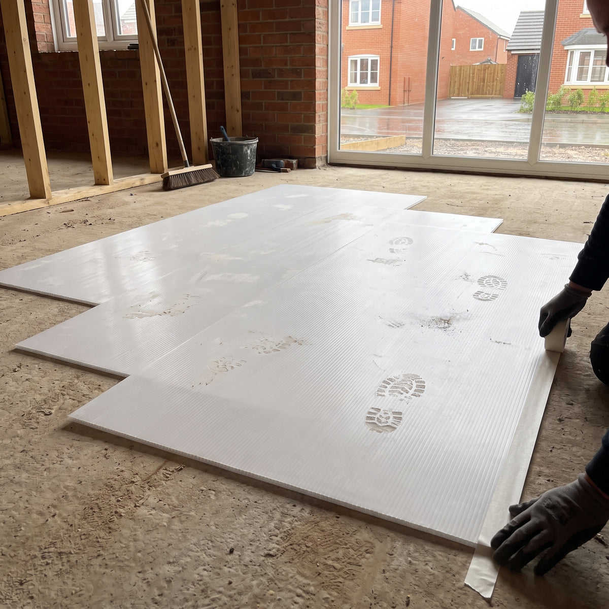 Full-size 2440 x 1220mm white fluted polypropylene sheets laid as floor protection on a new-build site